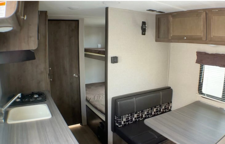 Single bowl sink, 2 gas burners & microwave above.  View of single over double bunks & fold down kitchen table to sleeper.