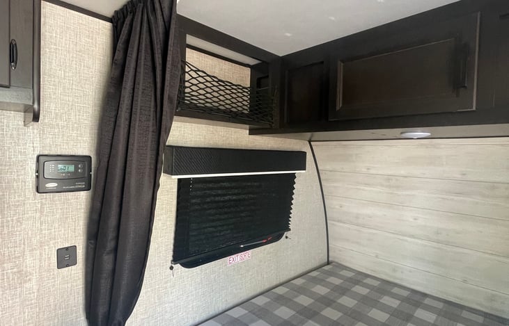 Queen bed upper net storage, storage cabinets above queen bed, window with black shutters, privacy curtain, thermostat next to curtain, all new.