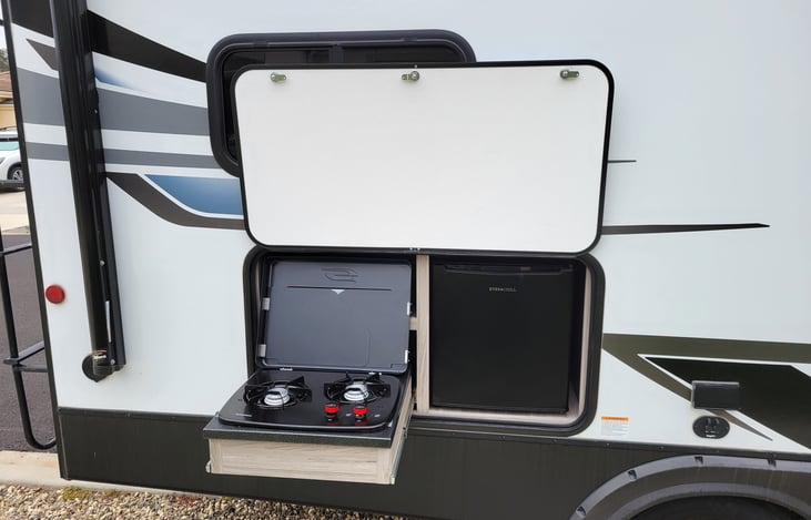 Outdoor kitchen with two burner stove and mini fridge.