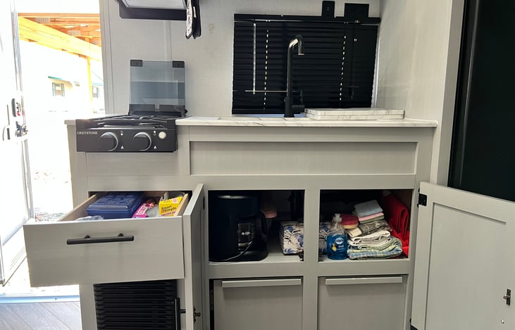 Kitchen cabinets and drawer stocked with towels, wash clothes, cutlery, a coffee machine and even some disposable kitchen basics