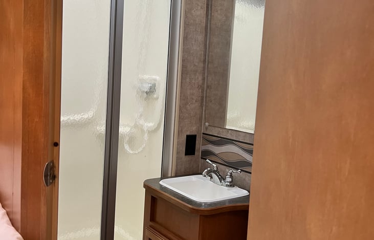 Three piece bathroom - toilet, sink, Stand up shower. Towel hooks and storage.