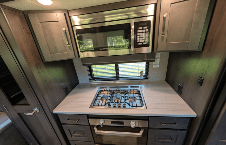 Gourmet galley & rear den retreat! Includes a 12 cu ft fridge, pantry, stove/oven, dual sofas, theater seats, 50" TV, electric fireplace, and 3 slides for spacious high-end living.