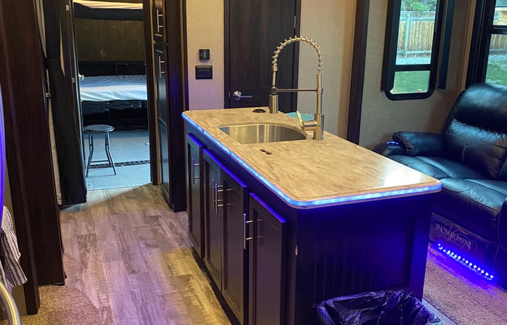 Kitchen island. Door is open to show the garage area and bunks. Loft is located above garage door. (Access loft by metal ladder). Partial bathroom is located between the garage and main living area.