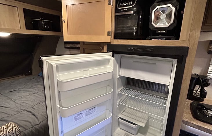 Refrigerator/ freezer and equipment stored overhead includes: air fryer, outdoor cordless light, Bluetooth party speaker, DVDs, playing cards, chess board, and video games.