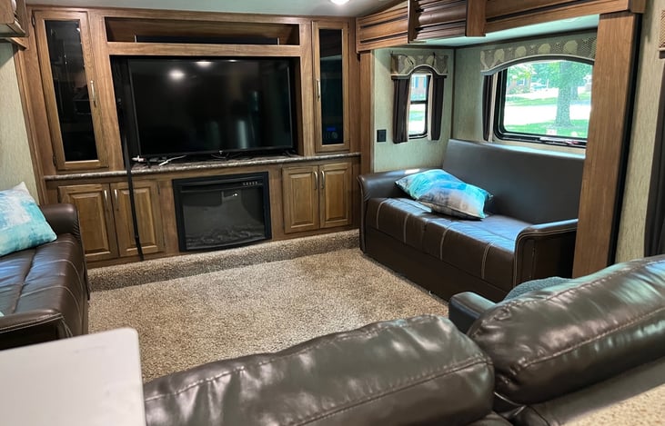 Full view of the front living room with dual reclining love seat facing the large screen smart TV.  Couches on each side fold to dual queen beds.