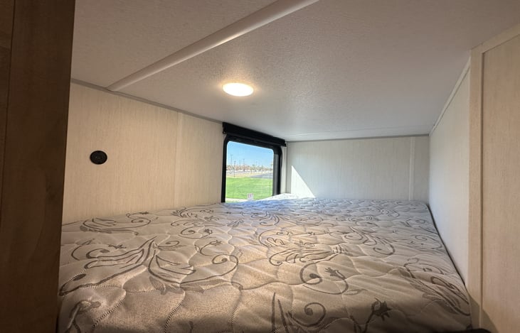 Rear bunk sleeping area with window and clean mattress surface.
