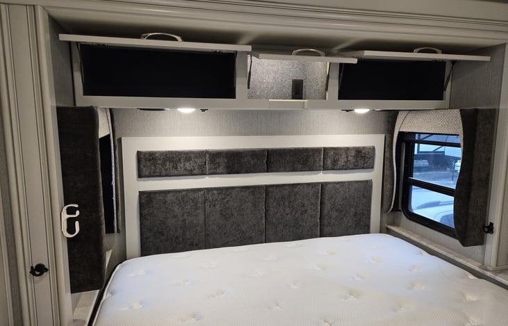 View of upgraded King Size bed in master bedroom area and overhead storage cabinets.