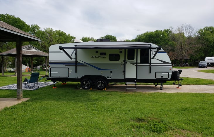 Campside of the travel trailer has a retractable awning, LED awning lights, LED underglow lights & an outside kitchen that has a refrigerator and blackstone-type griddle with outside cooking utensils