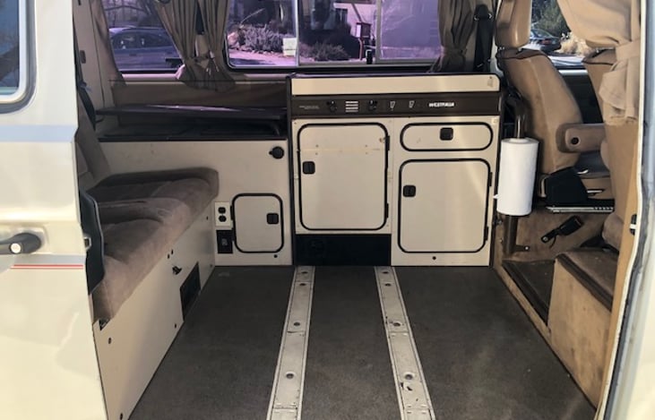 View of cook station from outside.  To the left of the cook station is a table that swivels out for use (height can be adjusted too).  White rails on floor can accommodate one or two extra seats.