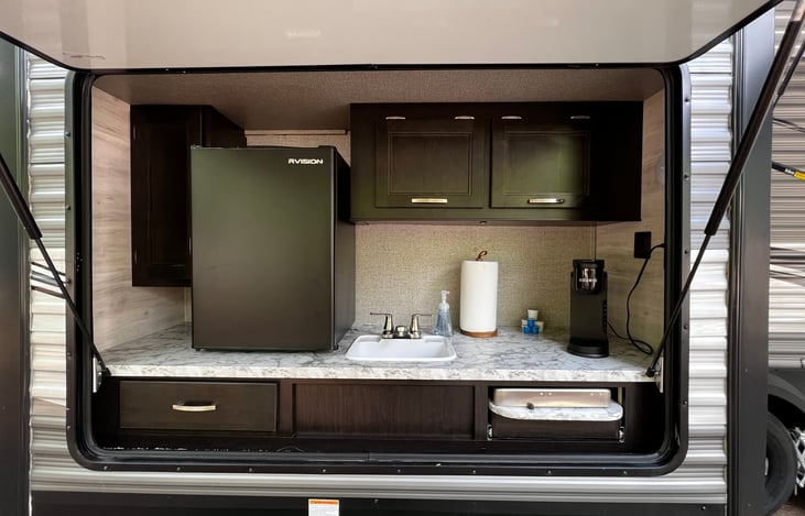 Outdoor kitchen with Keurig coffee maker, toaster, mini fridge, sink and 2 burner grill. Coffee cups included