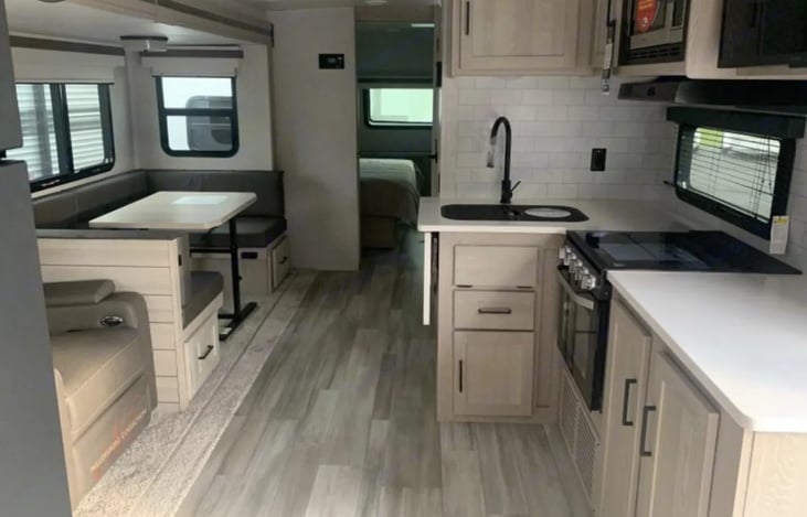 View from main doorway entrance. Loveseat faces mounted TV equipped with firestick and a cable cord. Gas range with oven for baking.