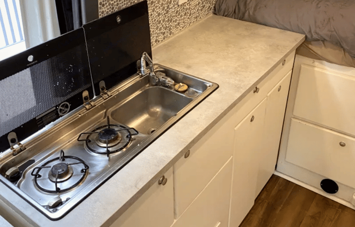 Kitchen includes Dometic 2 burner propane stove as well as sink. The sink drains into a 20 gallon grey water tank, under the vehicle.