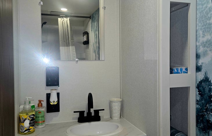 Sink in bathroom. Extra storage areas. Has hand soap, lotion, toothbrush holder, face soap. Barn door