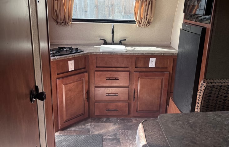 Has propane stove, microwave, refrigerator, and sink. Will provide some cooking pans, pots and some plastic ware. Has a pantry space and some cabinet storage.