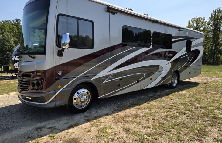 Driver side view with living room slide, electrical hookup, water hookup, generator compartments.