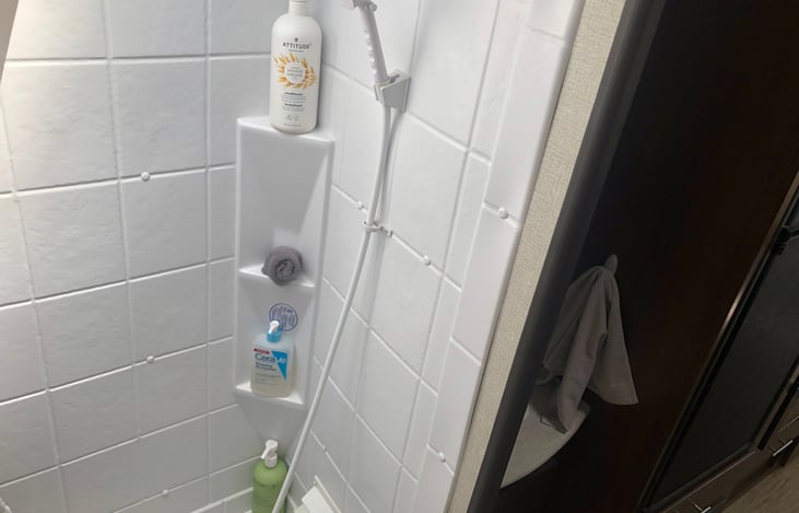 This show cases the size of bottle accommodated with in this snug space. It will fit regular size bottles but travel maybe the way to go. 
To use shower slide the towel cubby over toilet.