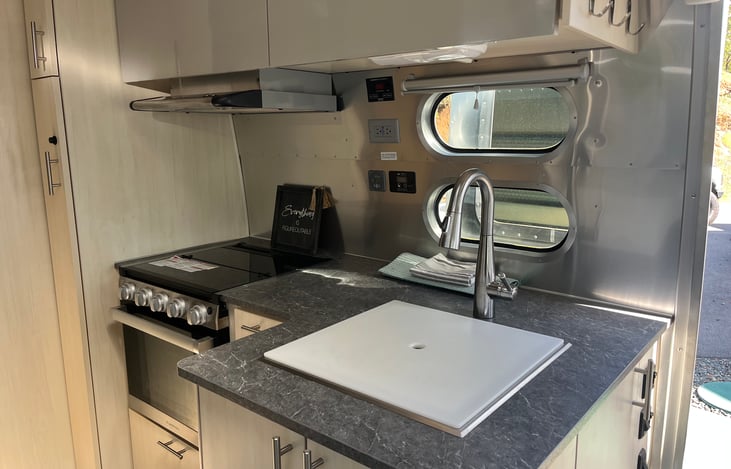 Kitchen with 3 burner propane gas stove and oven. Hood fan above.