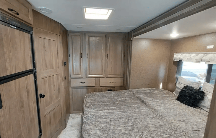 view from front to rear, primary queen size bed, storage closets, bathroom door, frig