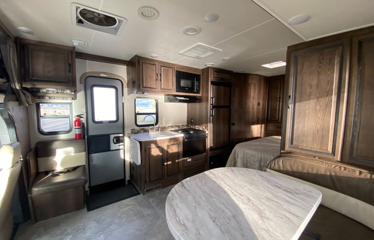 View from dinette. This shows the extra seat by door (under the fire extinguisher), the kitchen including relatively large sink, range, oven, microwave, and relatively large fridge and freezer.