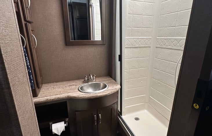 Bathroom with step flush toilet, sink, storage, and shower with hot water.