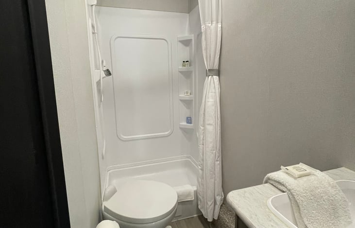 Bathroom features a tall shower, toilet, sink area, and upper and lower storage for all toiletries.
