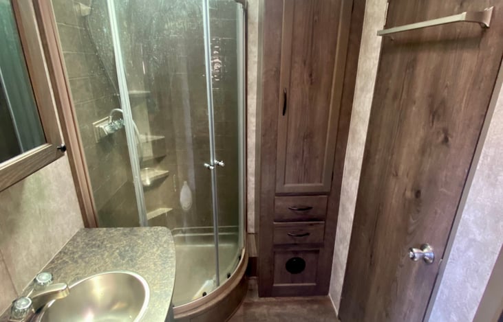 Bathroom with shower, sink, toilet and storage.