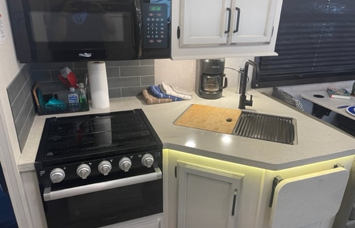 Kitchen area with double sink, cutting board, microwave, coffee pot, cabinets, drawers for utensils.