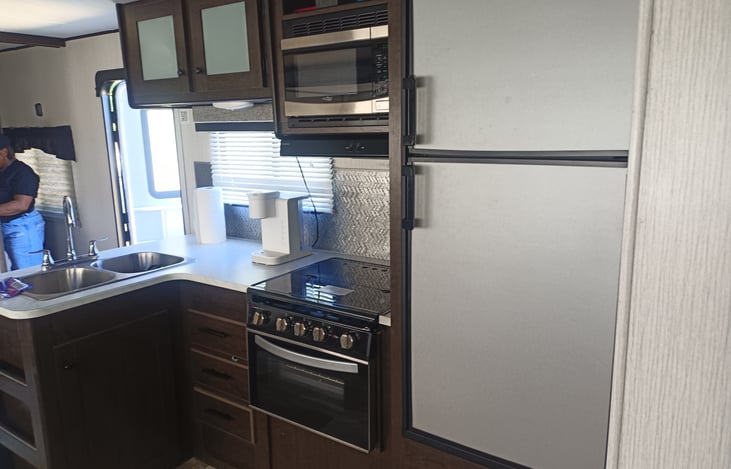 Indoor kitchen with kitchen sink, 3 cooking burners, refrigerator, microwave, and oven