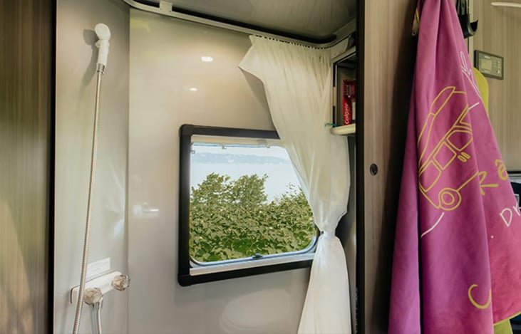 Another view of shower with hand-held shower head. Window has screen and / or blackout shade like all the rest. Also is covered with shower curtain.