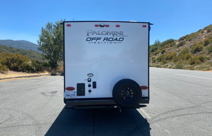 Rear view of trailer with outdoor shower, spare tire, and 30 amp hook up.