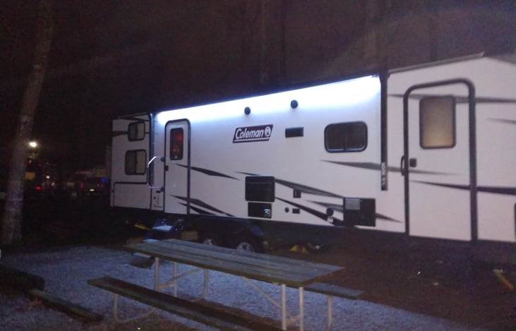 The LED lights adorning the sides and front of the camper create a warm, inviting glow, making it the perfect setting for unforgettable outdoor gatherings.