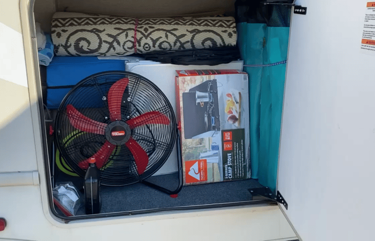 Large storage locker, complete with outdoor rug, four oversize chairs, camp stove, cooking table, fans, and rain/shade canopy