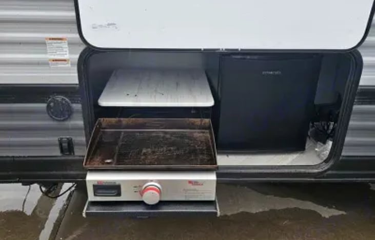 Outdoor kitchen with griddle and mini frig.