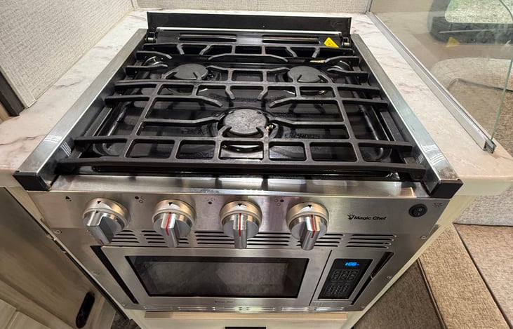 Three burner kitchen propane stove. Below is a microwave/convection oven.