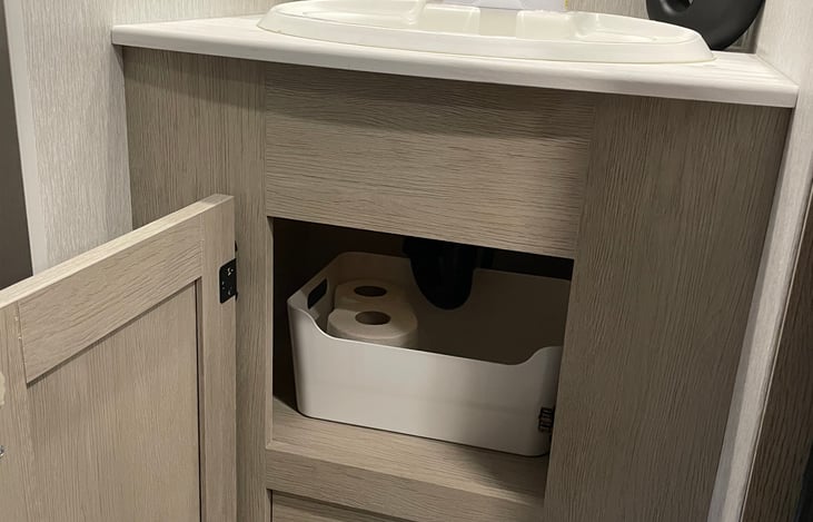 UNDER SINK STORAGE WITH INCLUDED TOILET PAPER.
