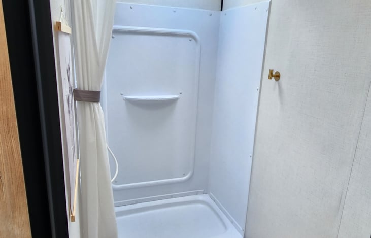 Bathroom shower, with a gold hook to hang your wet towel.