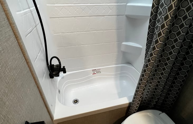 Bathroom with full size RV tub, toilet, overhead vent, skylight and curtain.