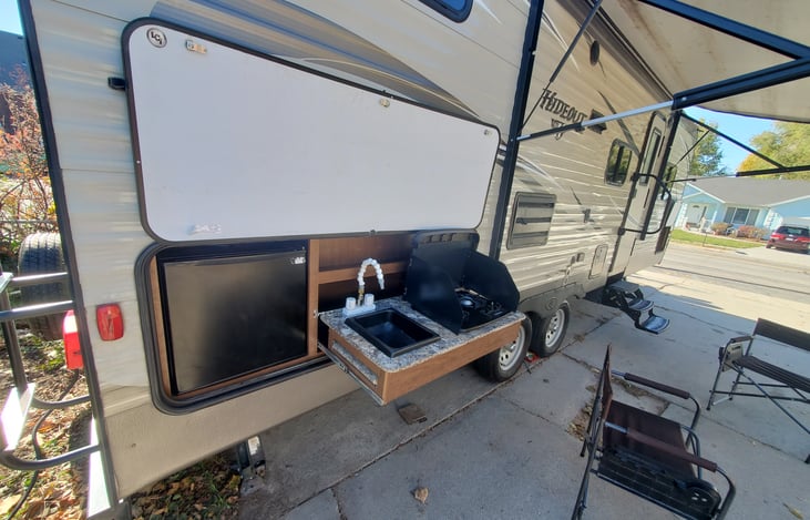 Outdoor kitchen has sink, stove, and a fridge