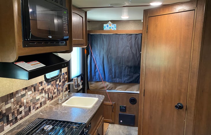 Looking to the rear of the trailer, you can see the entryway, kitchen and bathroom.  The kitchen includes a microwave, sink, stove and oven.
