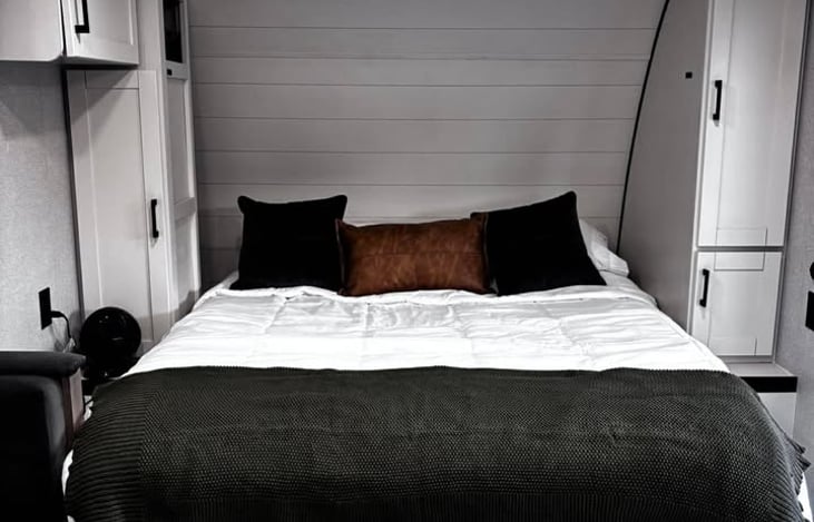 A cozy, modern RV bedroom featuring a plush queen bed, warm lighting, and smart built‑in storage for a comfortable stay.