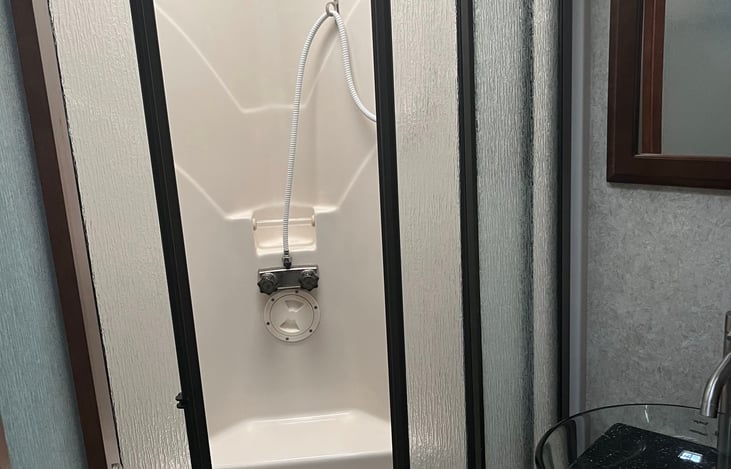 Enjoy the comfort of a spacious walk-in shower with glass doors, a built-in seat, and skylight above—offering plenty of headroom, natural light, and a relaxing, spa-like experience on the road.