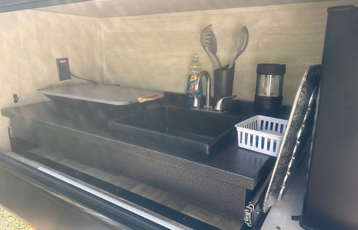 Outdoor kitchen includes small refrigerator and movable sink