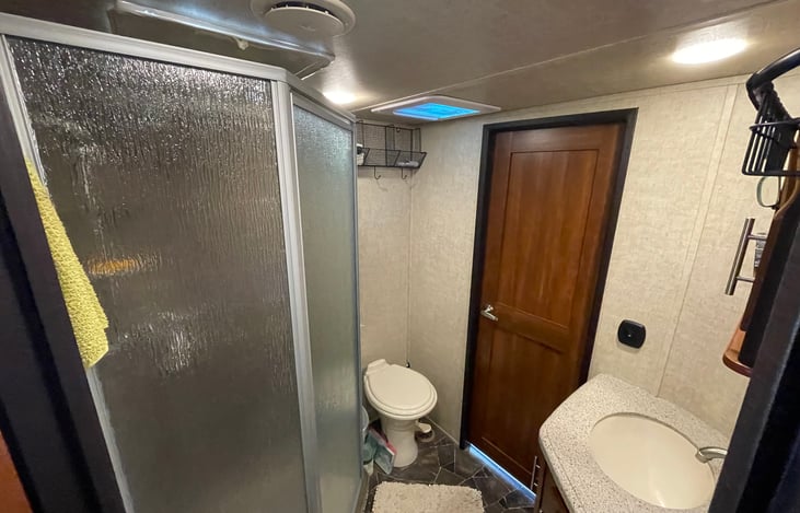 Bathroom with toilet, sink, shower and 2 entry doors.