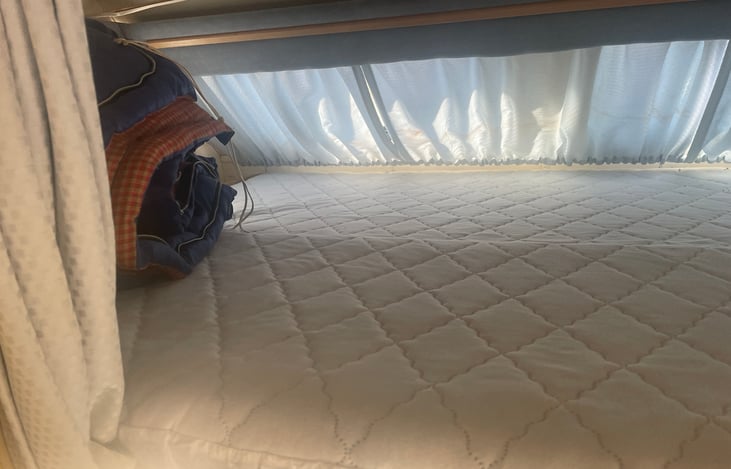 The cozy top bunk is a queen sized bed. It features a reading light and storage along the edges of the mattress.