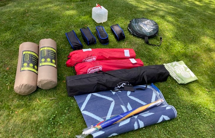 Rental includes everything in photo:  2 ground mats (tan), 4 chairs, water container, collapsible trash can , 2 captain chairs (red), large tent canopy (long black), rug, umbrella, and table cloth