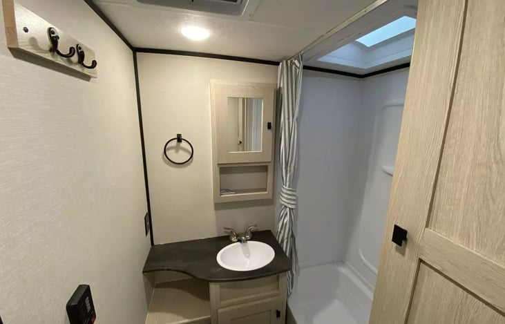 View into spacious bathroom with sink and mirrored medicine cabinet and shower with skylight