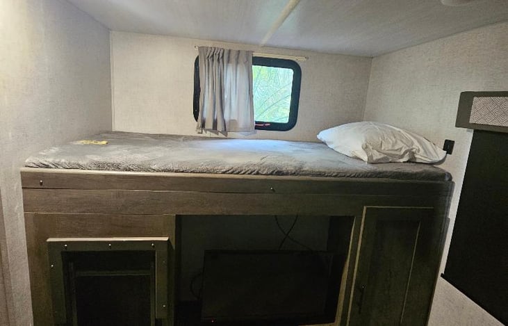 Bunkroom with top bed and TV, ladder.
