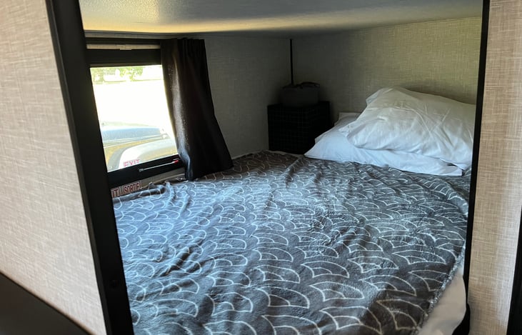 Bottom bunk, full size, includes emergency window, bedding, two pillows, electronic outlet, individual lighting, and storage cubby.