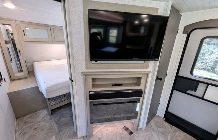 Bright and modern interior with a Custom King bed, double bunks, and a Versa-Lounge slide. Features a 30” fireplace, panoramic windows, 10.7 cu ft fridge, and a walk-in closet. Luxury camping at its f