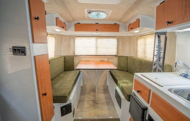This photo shows the table up configuration for enjoying meals inside the Scamp. You can see the cutting board that covers the sink and the glass cover over the propane cooktop burners